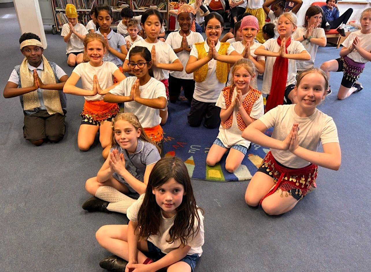 Children sit with their palms pressed together smiling to camera