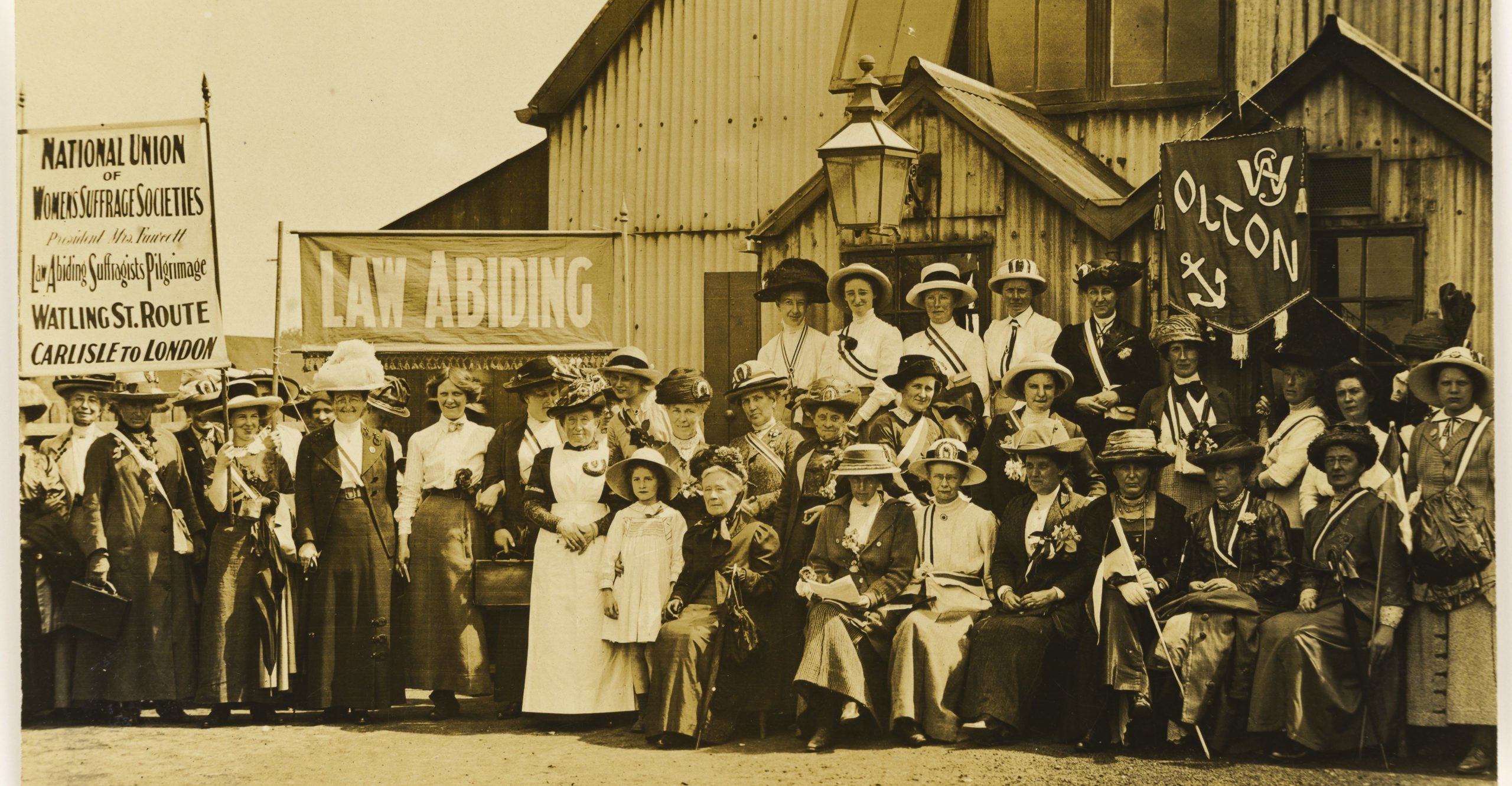 Many Suffragettes hold banners ready for a march