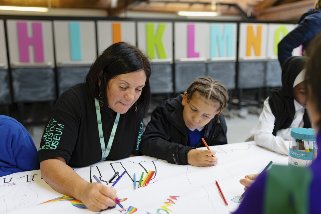 Woman sits with a young boy, both drawing