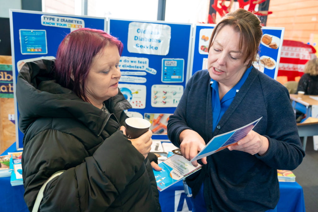 A nurse showing some information to a lady who is holding a cup