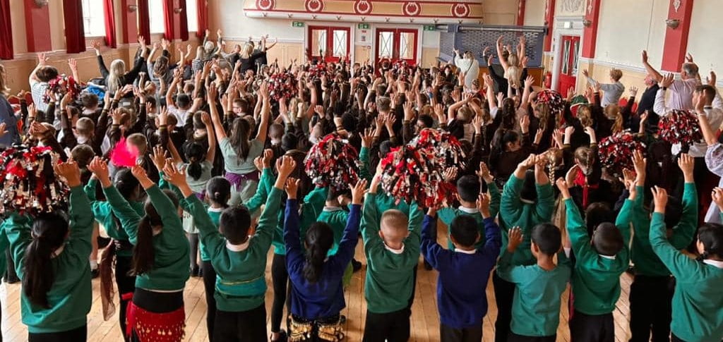 A school full of children with their arms in the air, waving pompoms