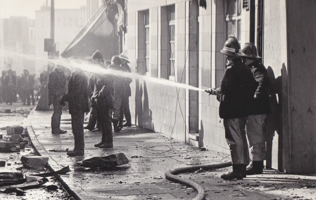 Photograph of fire fighters using a water hose to put out the fire at Victoria Market Hall.