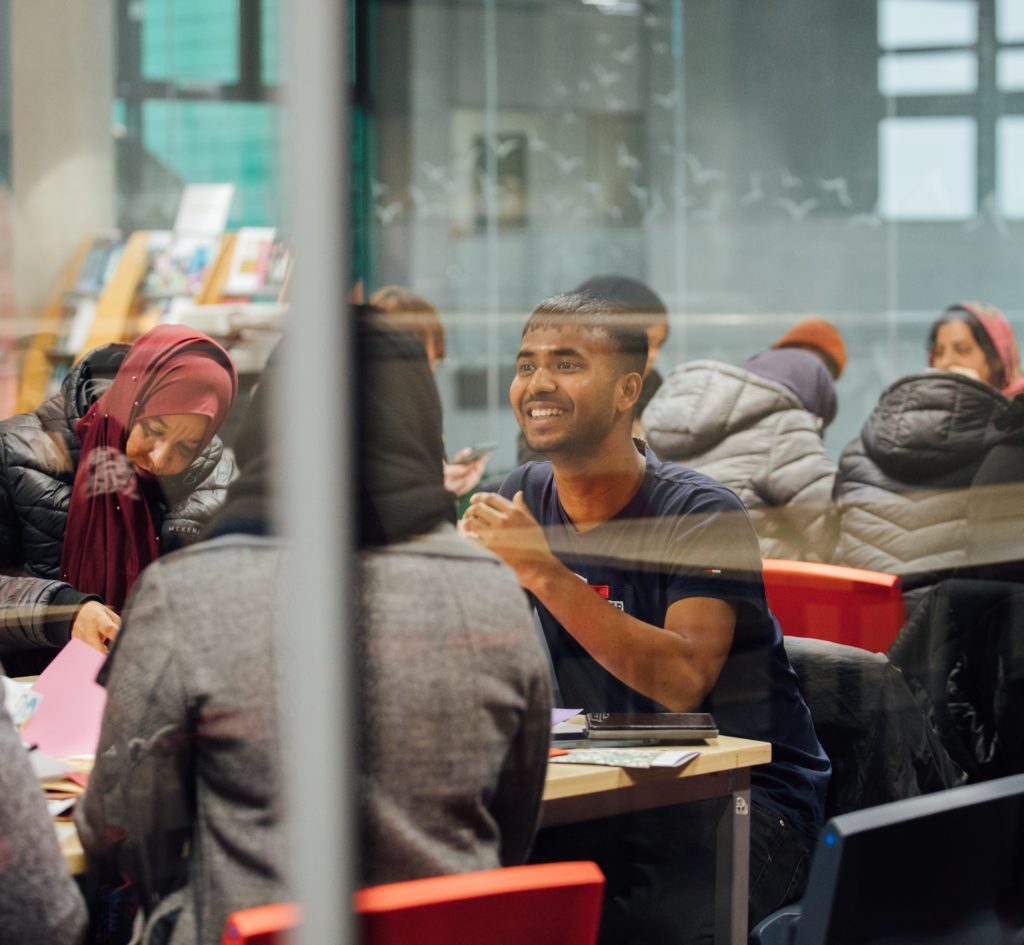 A group of people chatting and working in a glass-walled room