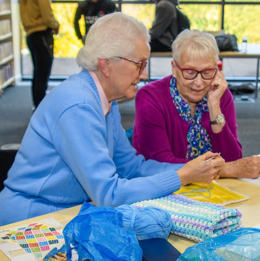 Two ladies wearing glasses looking at a crochet blanket.