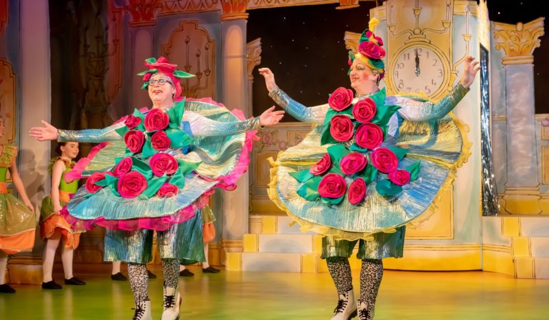 Two actors in outrageous costumes with huge roses on the front on the set of Cinderella from 2018.