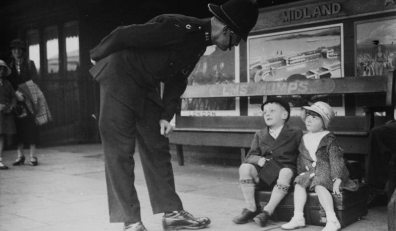 Policeman looking down at two children sat on a bench at Oldham Mumps train station.