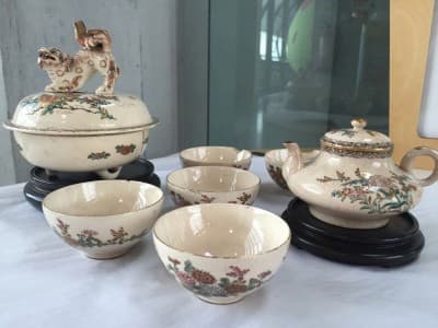 Japanese ceramics in museum display case. Cream-coloured teapot and drinking cups with floral pattern in pink and green, with gold decoration