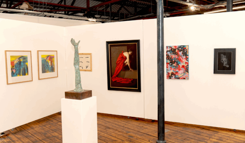 A view of the inside of 1853 Studios, with 6 artworks of various sizes on the wall and a sculpture on a plinth.