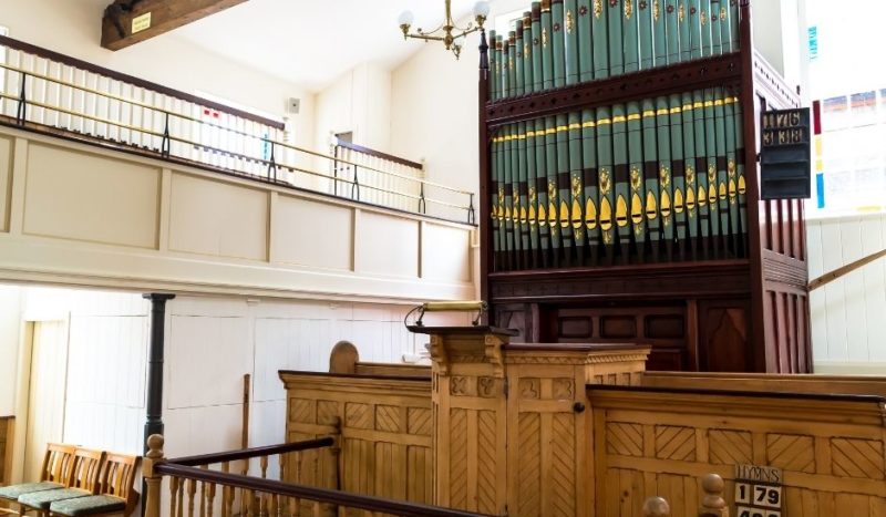 Photograph of the interior of George Street Chapel, with the large dark wood, blue and gold organ as the centre focus behind the altar.