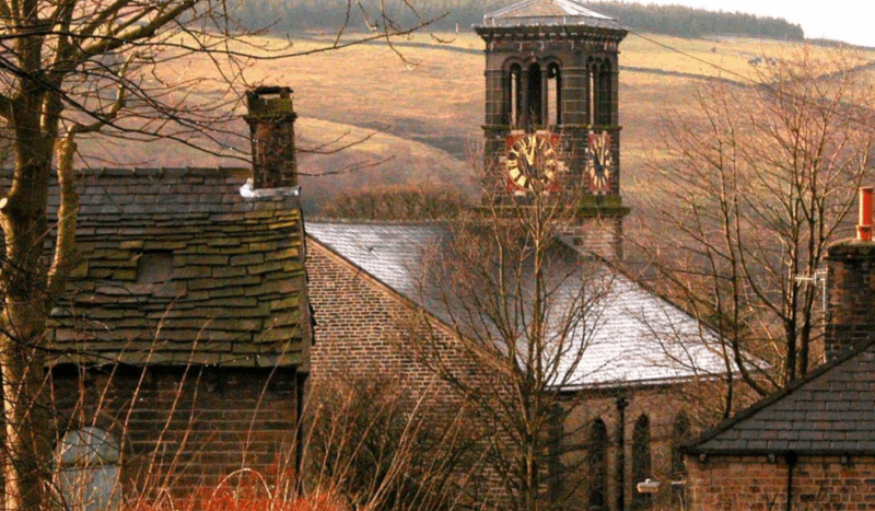 Autumnal photograph of Holy Trinity Dobcross with the clock tower in the background centre.