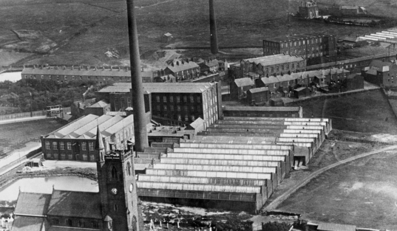 A black and white aerial view photograph of Moorside with the church and mills in focus.