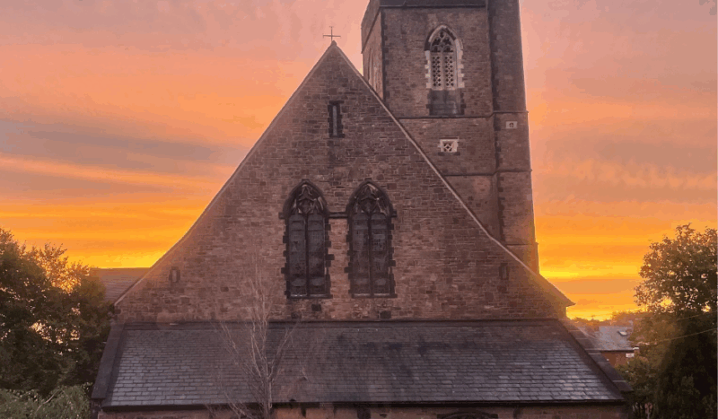 Photograph of St. Anne's Church in Royton with a lilac, pink and orange sky above