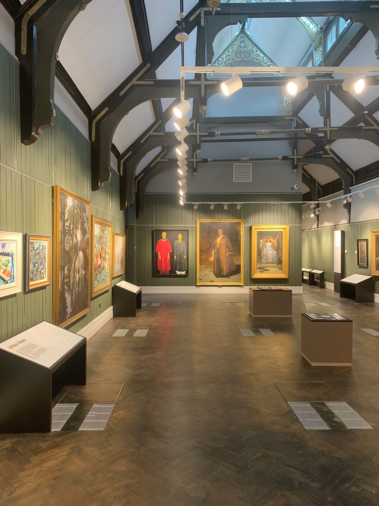 Photo of the art gallery showing 3 portraits on the back wall and the black and gold roof.