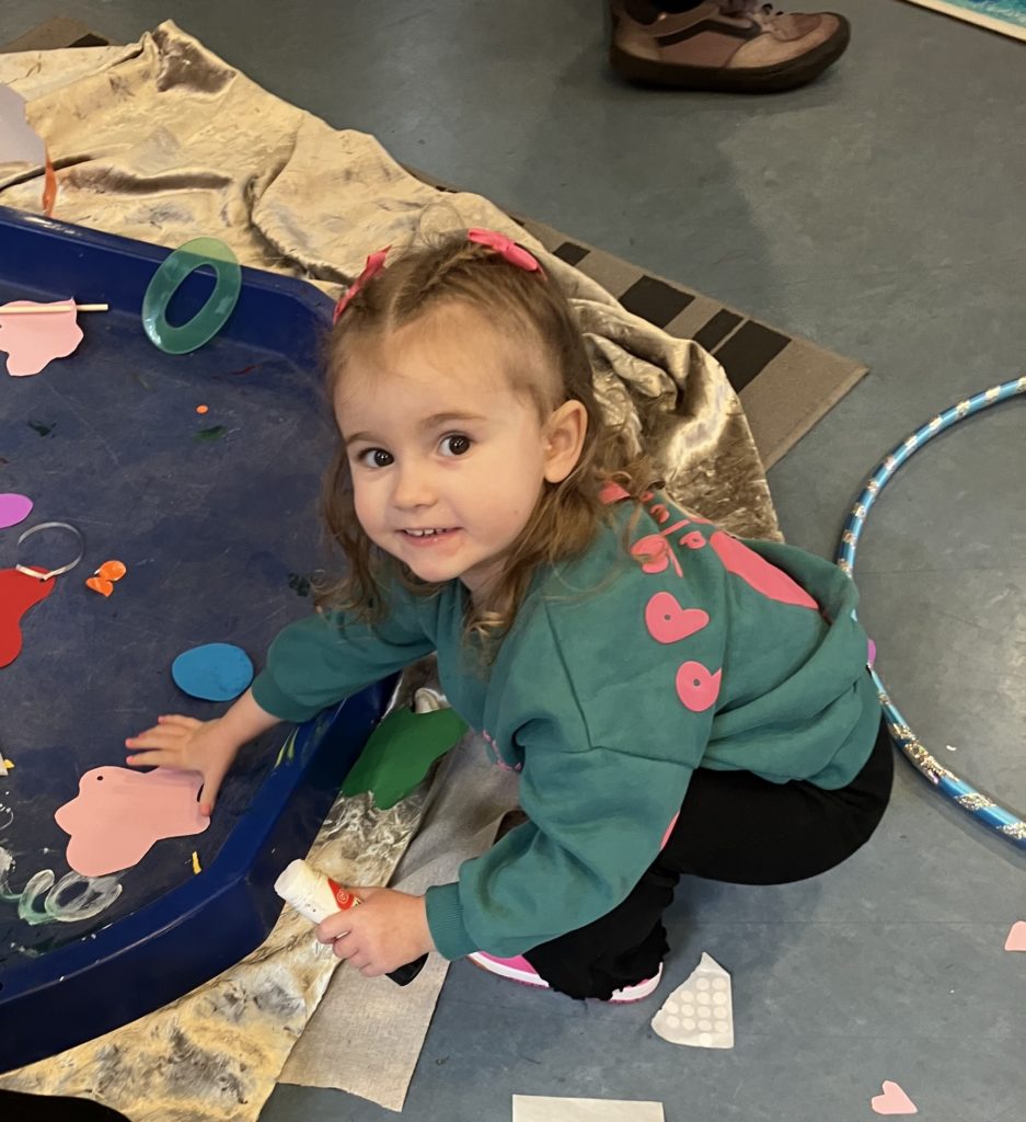 A small girl leaning over a tray of craft materials