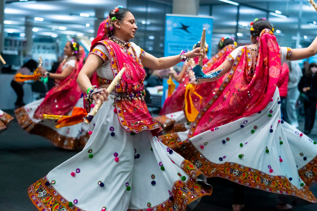 Some ladies dancing wearing colourful costumes. They are holding decorated sticks