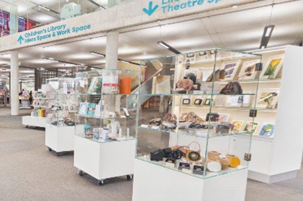 Some stands on a grey carpeted area with lots of items on display underneath some library signs