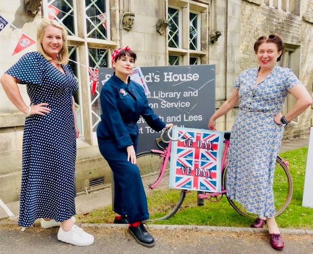 3 ladies dressed in 1940s clothes with a VE day sign