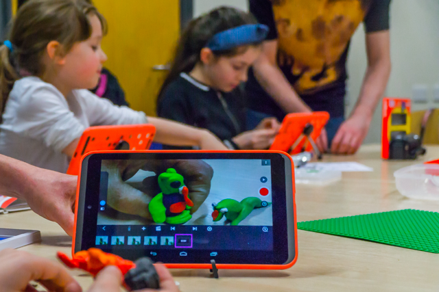A tablet in the foreground shows a hand moving a figure as part of a stop motion animation workshop