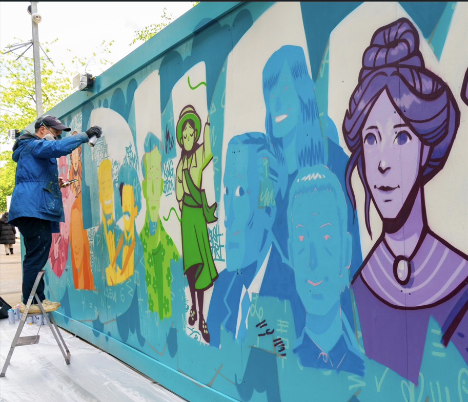 A man painting a wall with suffragette images in the word 'Oldham'