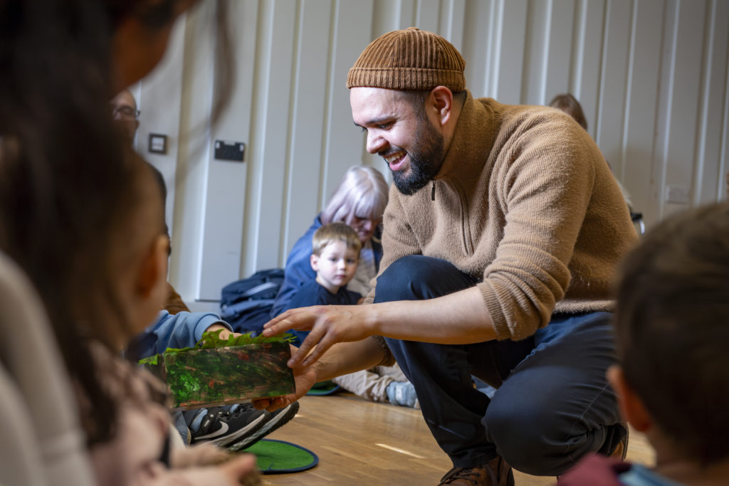 smiling man playing with early years telling them a story